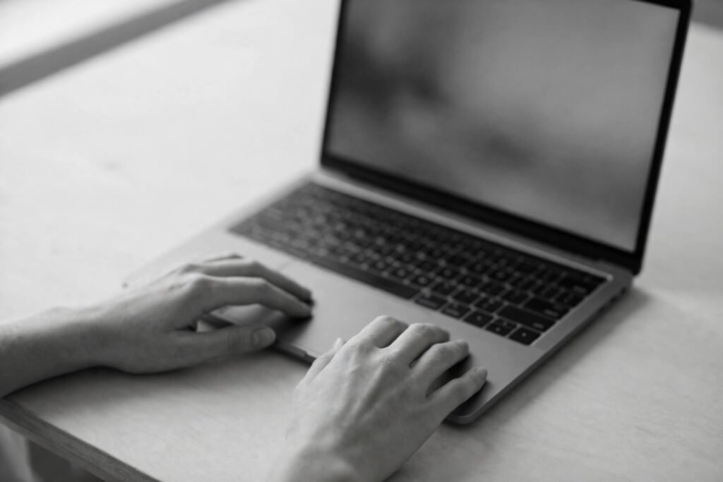 Hands reviewing a laptop at a clean desk in soft grayscale, illustrating a marketer reviewing AI-generated content