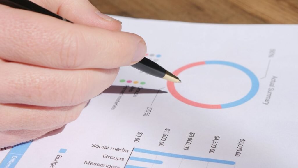 A hand holding a pen pointing at a printed chart with budget and channel data during analysis
