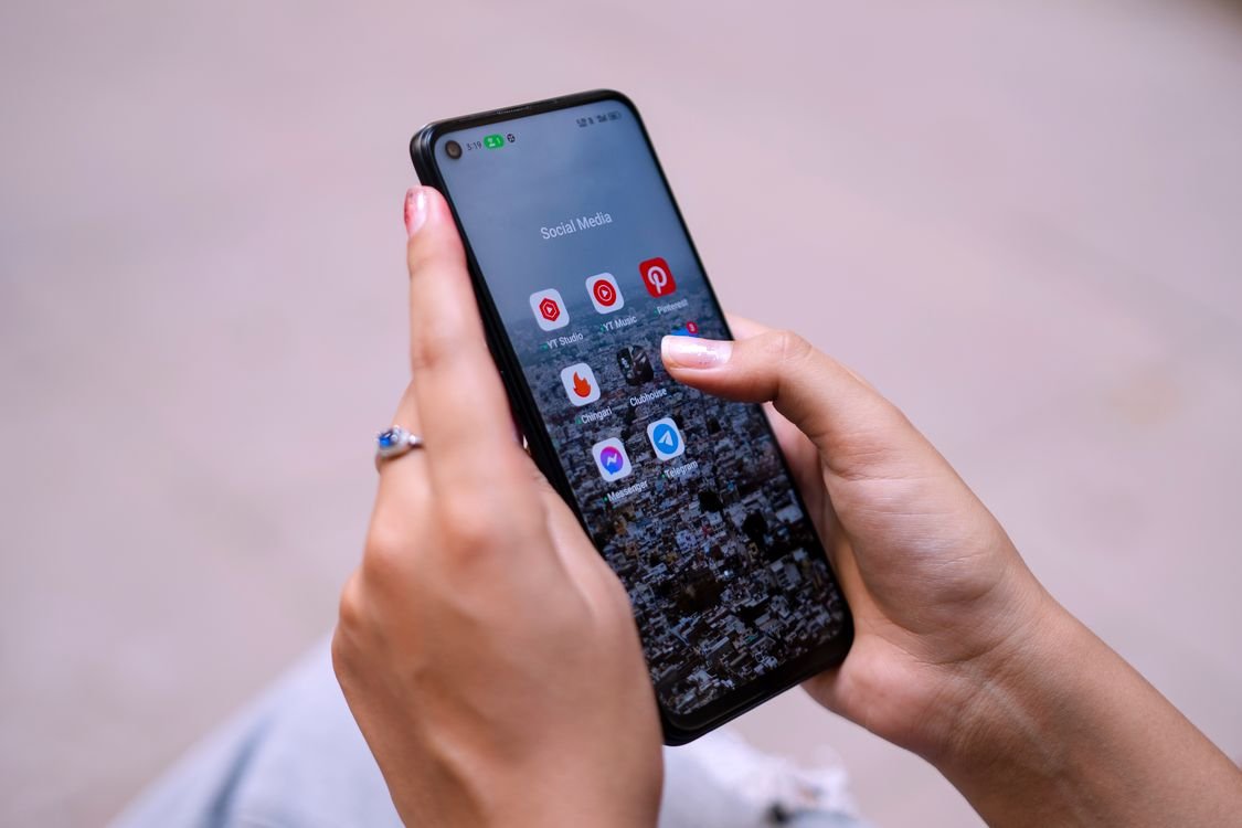 Hands holding a smartphone showing a social media app folder on the home screen